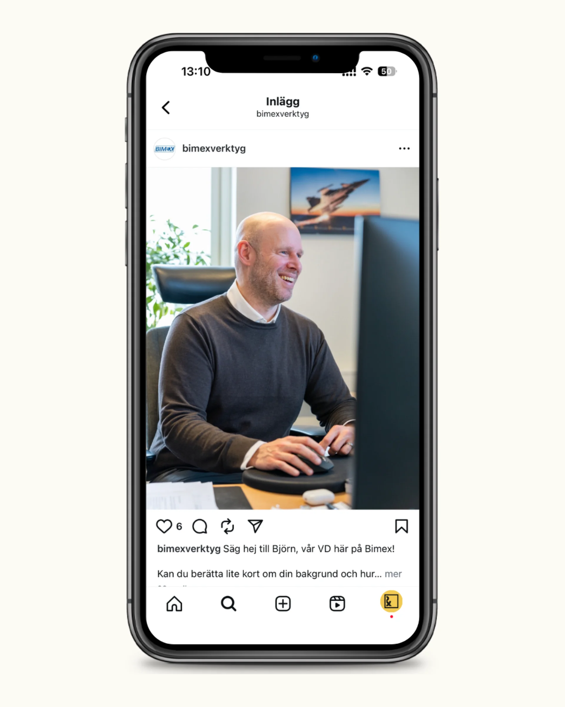 En leende, skallig man i grå tröja och vit skjorta sitter vid ett skrivbord och använder en dator i ett ljust kontor. Bilden visas på en smartphoneskärm som ett Instagram-inlägg.