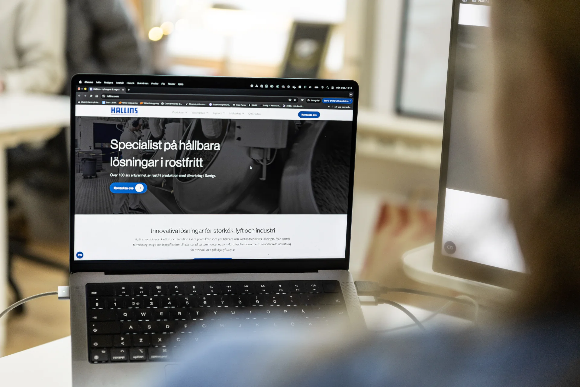 En person använder en bärbar dator som visar Hallins webbplats, som innehåller information på svenska om hållbara lösningar i rostfritt stål. Skärmen visar ett blått och vitt gränssnitt för webbsidor.