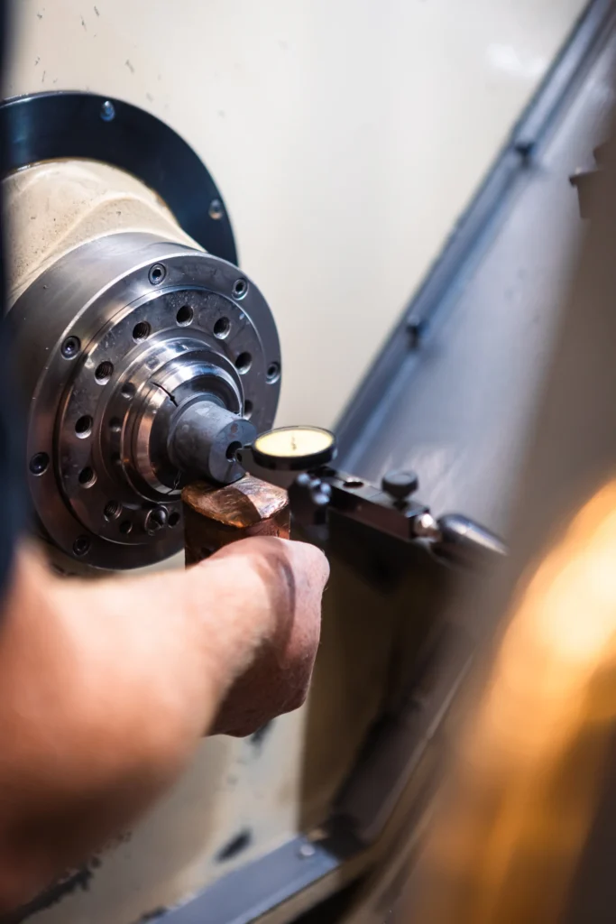 En närbild av en persons hand som justerar en metalldel i en svarvmaskin, med en mätklocka för exakta mätningar, visar det precisionsarbete som utförs i kundcase Hallins.