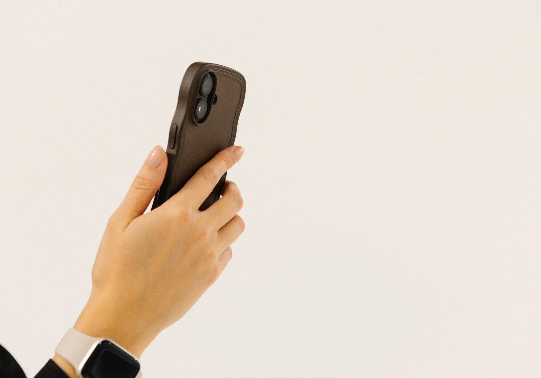 Mobil En person håller i en smartphone med mörkt fodral och har en smartklocka på handleden mot en vit bakgrund.