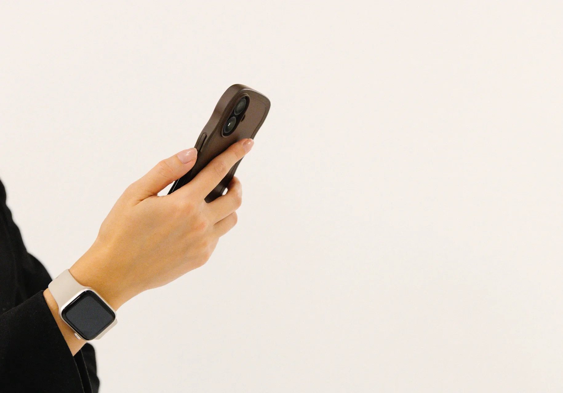 Sociala medier - Reklam & Co En person som bär en smartklocka håller en smartphone i vänster hand mot en vit bakgrund. Endast handen och en del av armen är synliga.